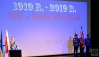 przemawiający na scenie komendant powiatowy policji, po drugiej stronie stojący ze sztandarem policjanci