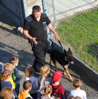 policjant prowadzący psa służbowego idący obok stojących dzieci