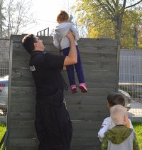 policjant trzymający dziecko nad przeszkodą przez którą skakał pies