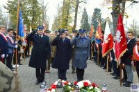 komendant policji w Kluczborku w obecności dwóch przedstawicieli służb mundurowych oddający honor przed pomnikiem Żołnierza Polskiego