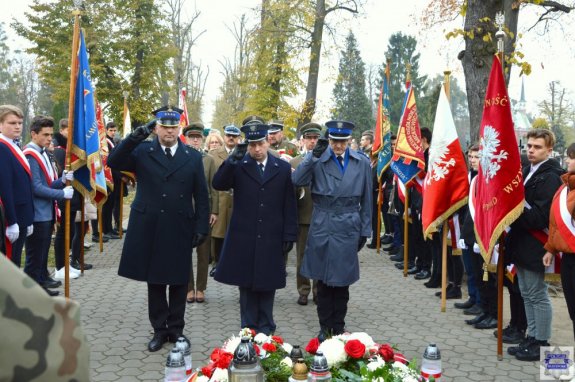 komendant policji w Kluczborku w obecności dwóch przedstawicieli służb mundurowych oddający honor przed pomnikiem Żołnierza Polskiego